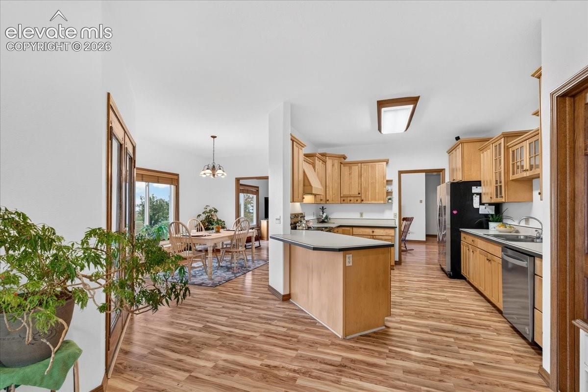 Kitchen featuring wood cabinetry, a center island with a solid surface countertop, wood-finish flooring, and a stainless steel dishwasher