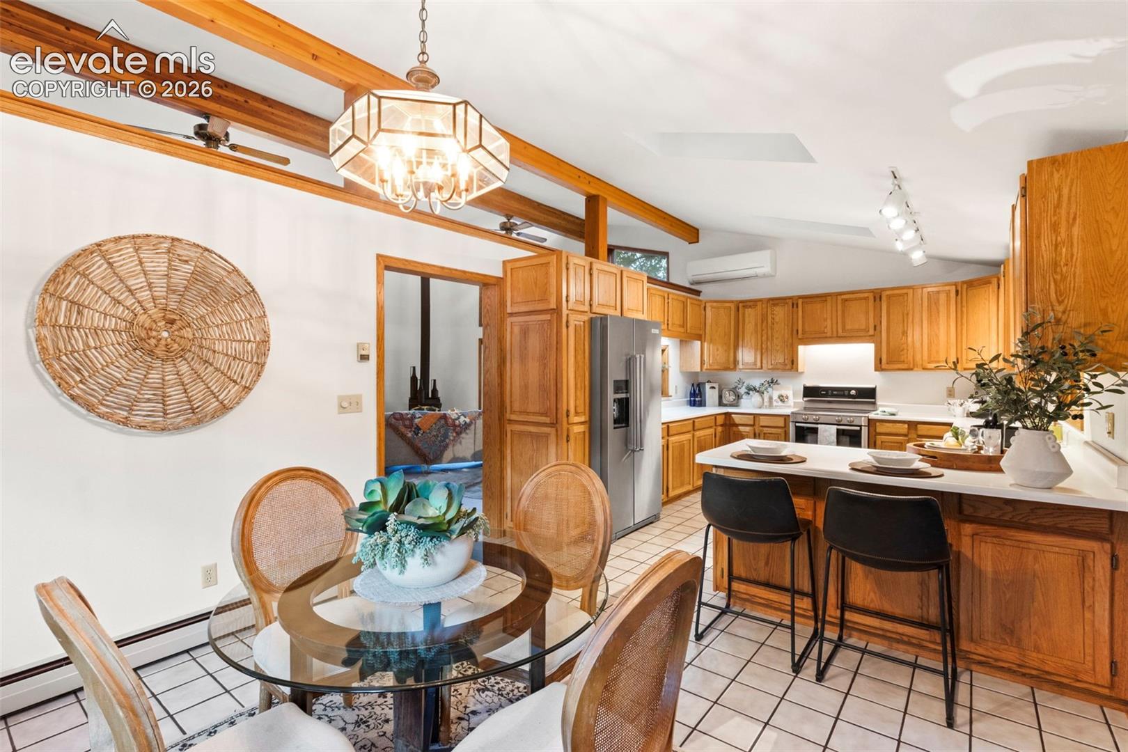 Vaulted ceiling with exposed wood beams, tiled flooring, cabinetry with wood finish, breakfast bar, and pendant lighting
