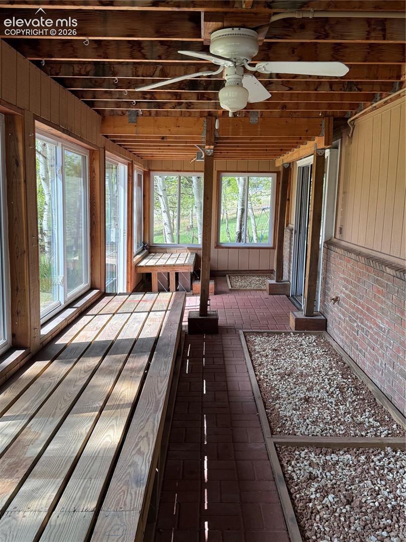 Enclosed porch featuring wood plank flooring, brick paver accents, exposed wood beam ceiling, multiple windows, and a ceiling fan