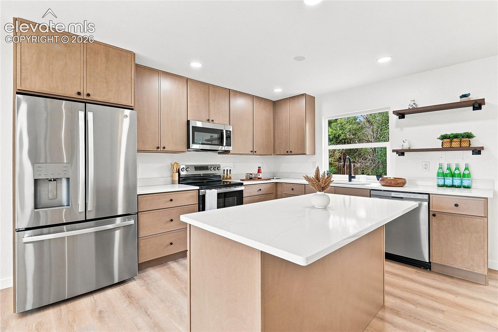 Contemporary kitchen featuring light wood-finish cabinetry, stainless steel appliances, white countertops, and wood-finish flooring