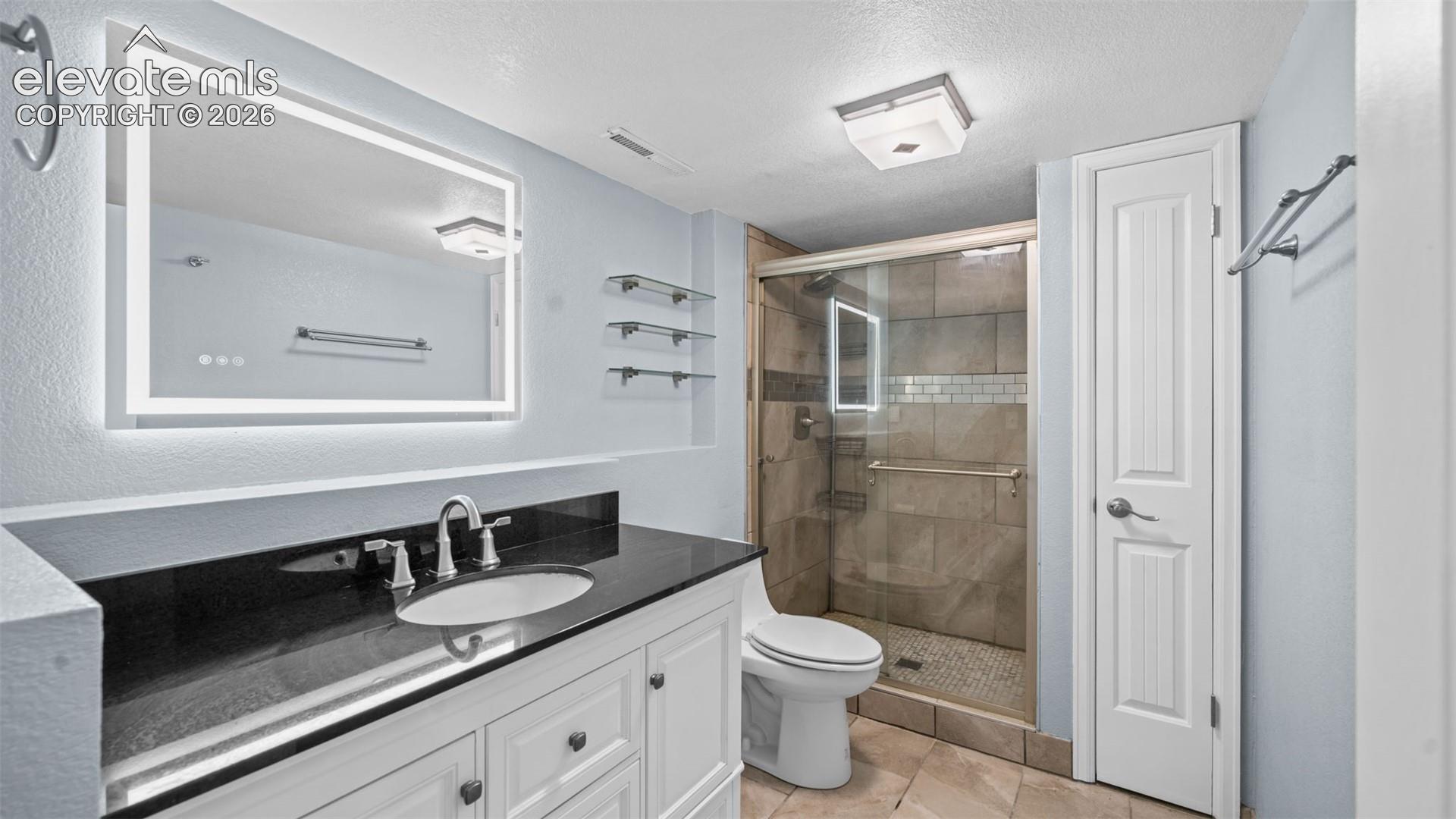 Bathroom featuring a white vanity with dark countertop, illuminated mirror, and glass-enclosed shower with tile surround