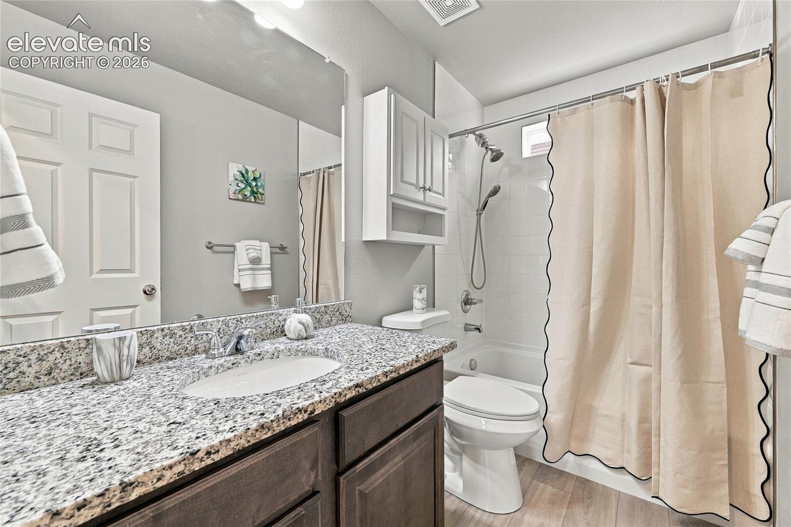 Granite countertop vanity with integrated sink, wood-finish cabinetry, and a full-width mirror