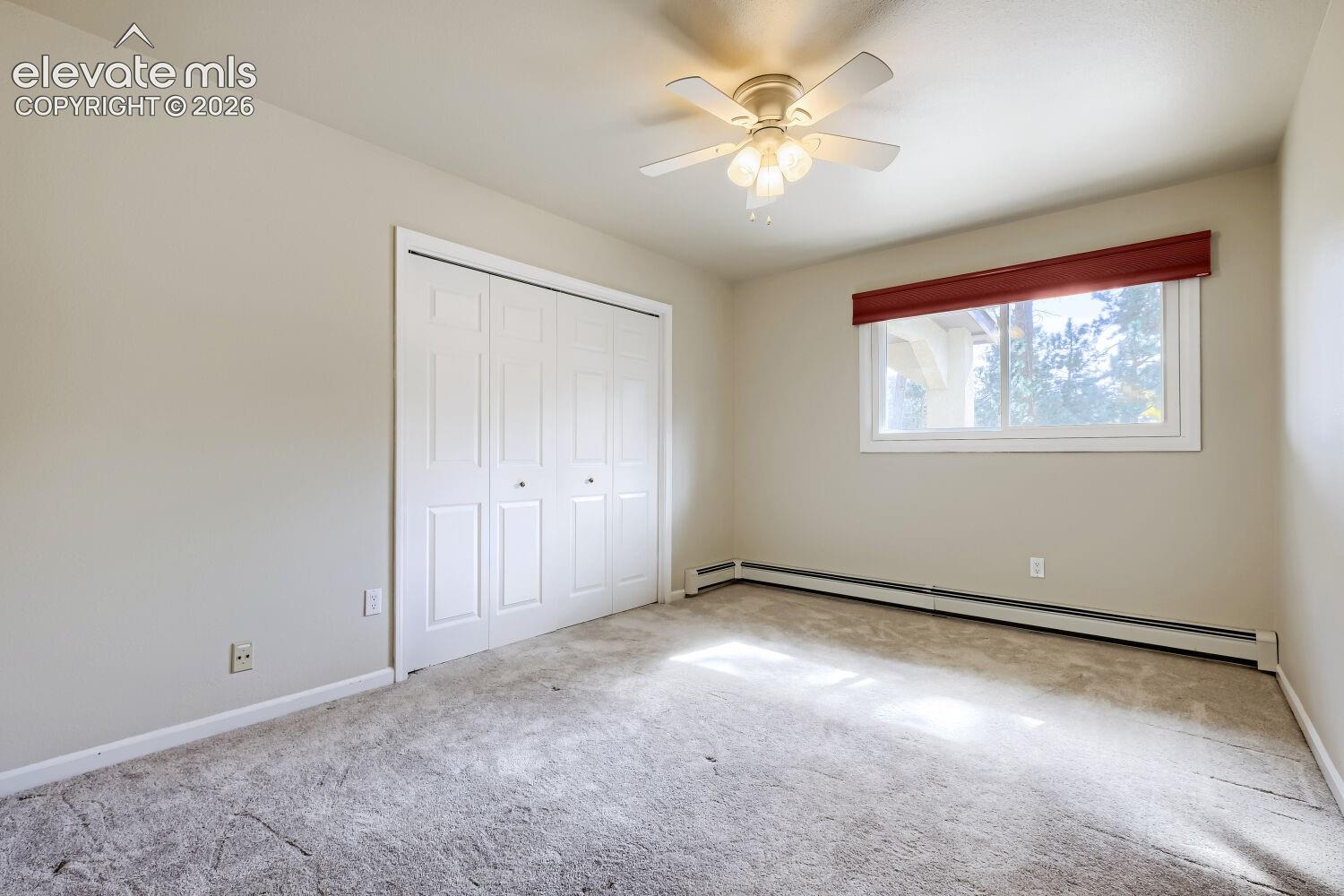 Carpeted room with a ceiling fan, a window with a red valence, and bi-fold closet doors