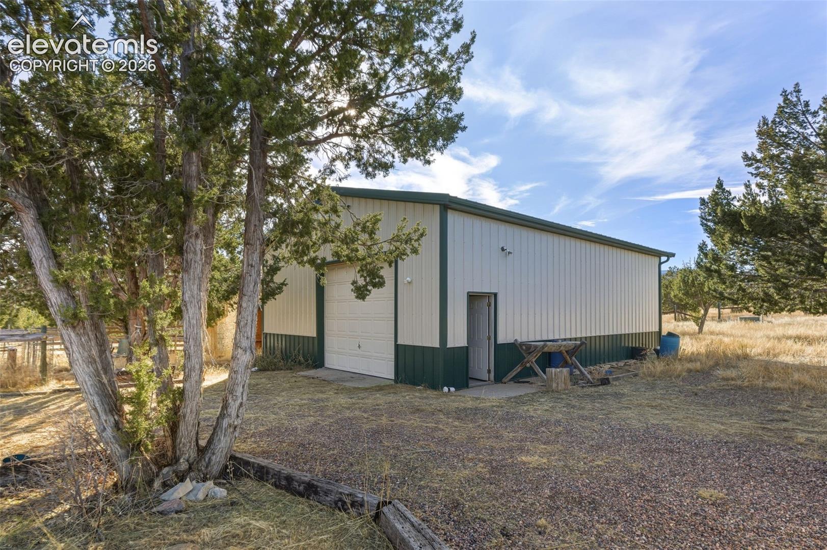 Metal structure with a rolling garage door, pedestrian door, and a gravel surface