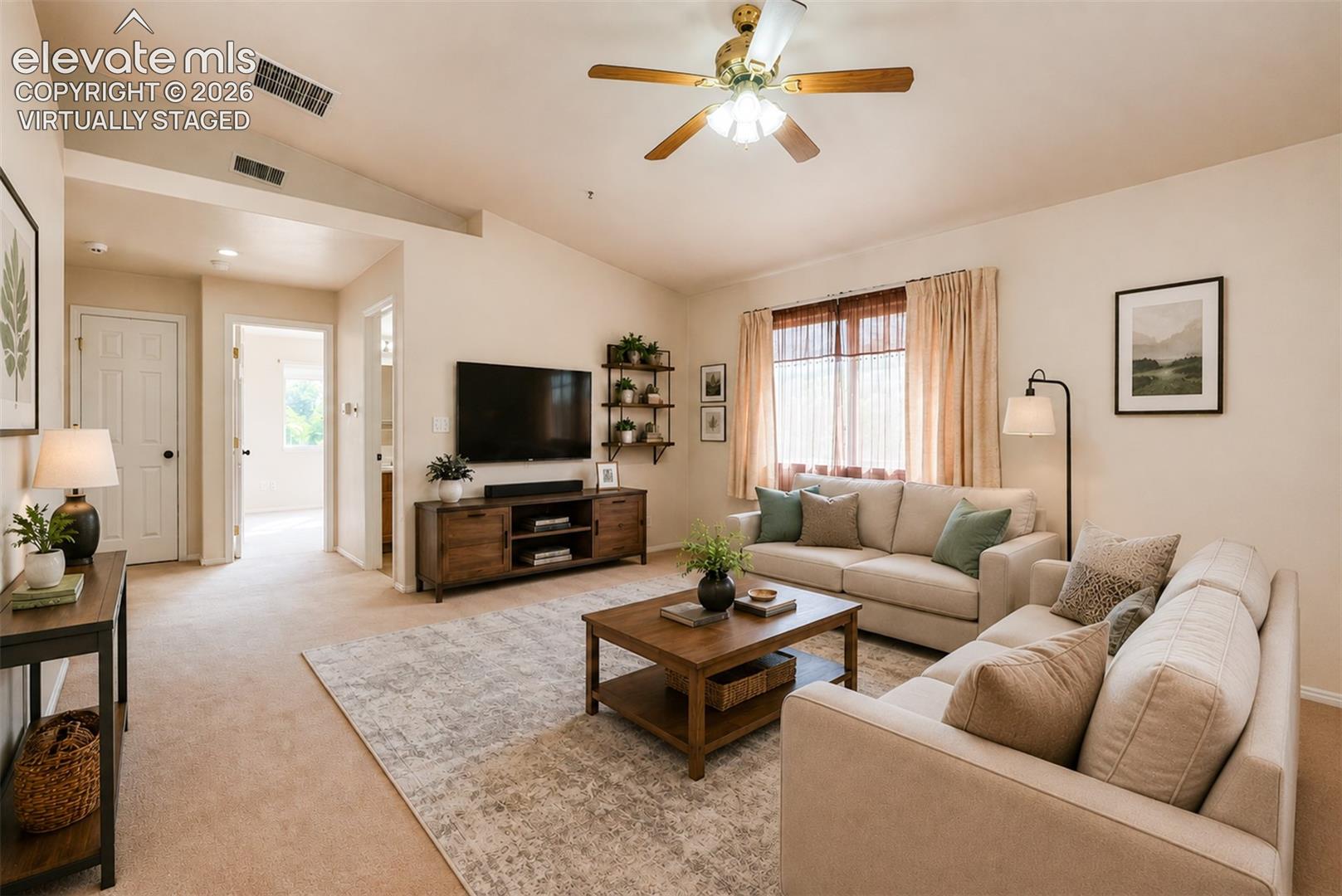 Living area featuring vaulted ceilings, neutral Virtually Staged tones, carpeted flooring, and a ceiling fan with integrated lighting