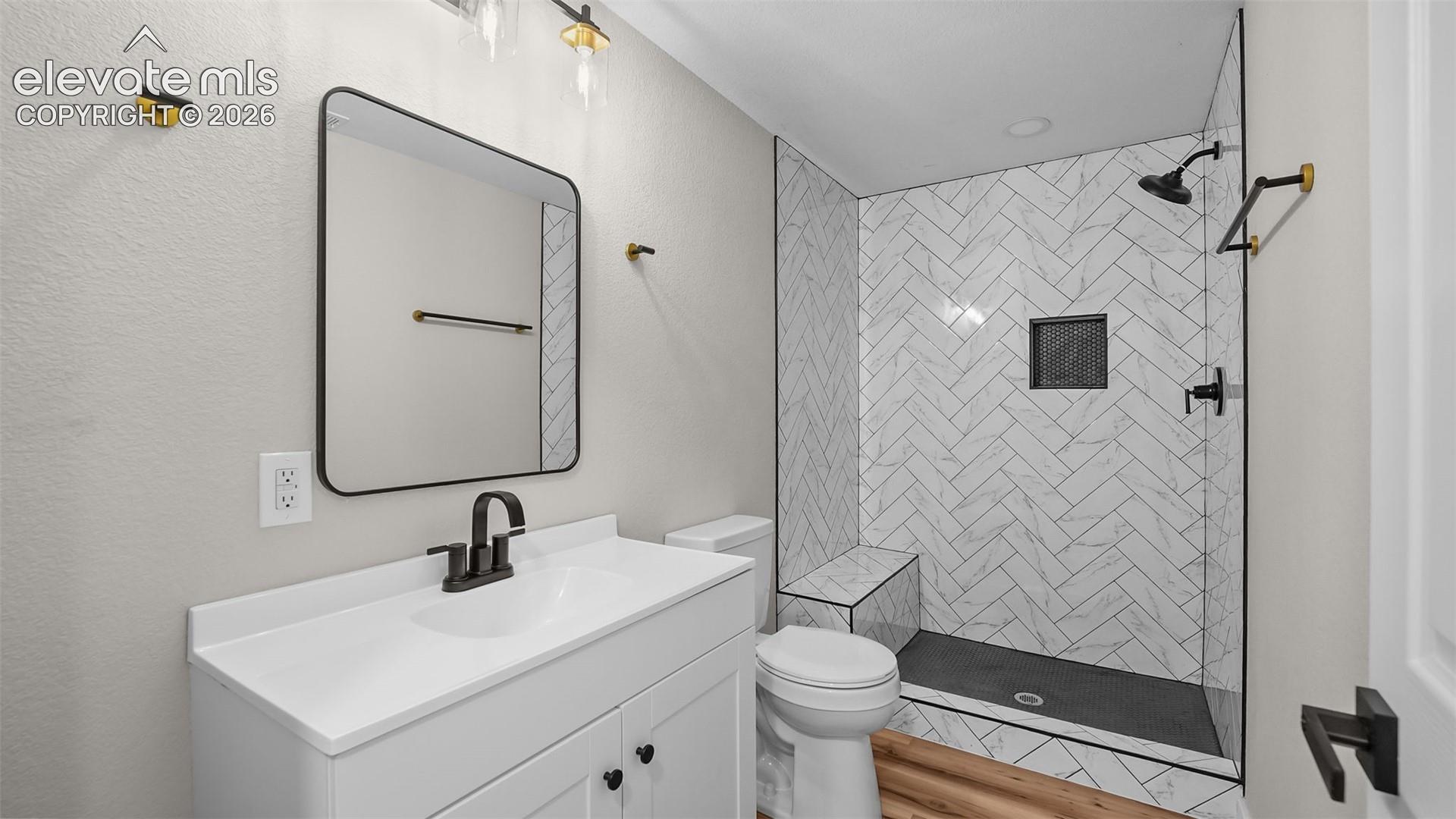 White vanity with black hardware, rectangular framed mirror, and wood-finish flooring