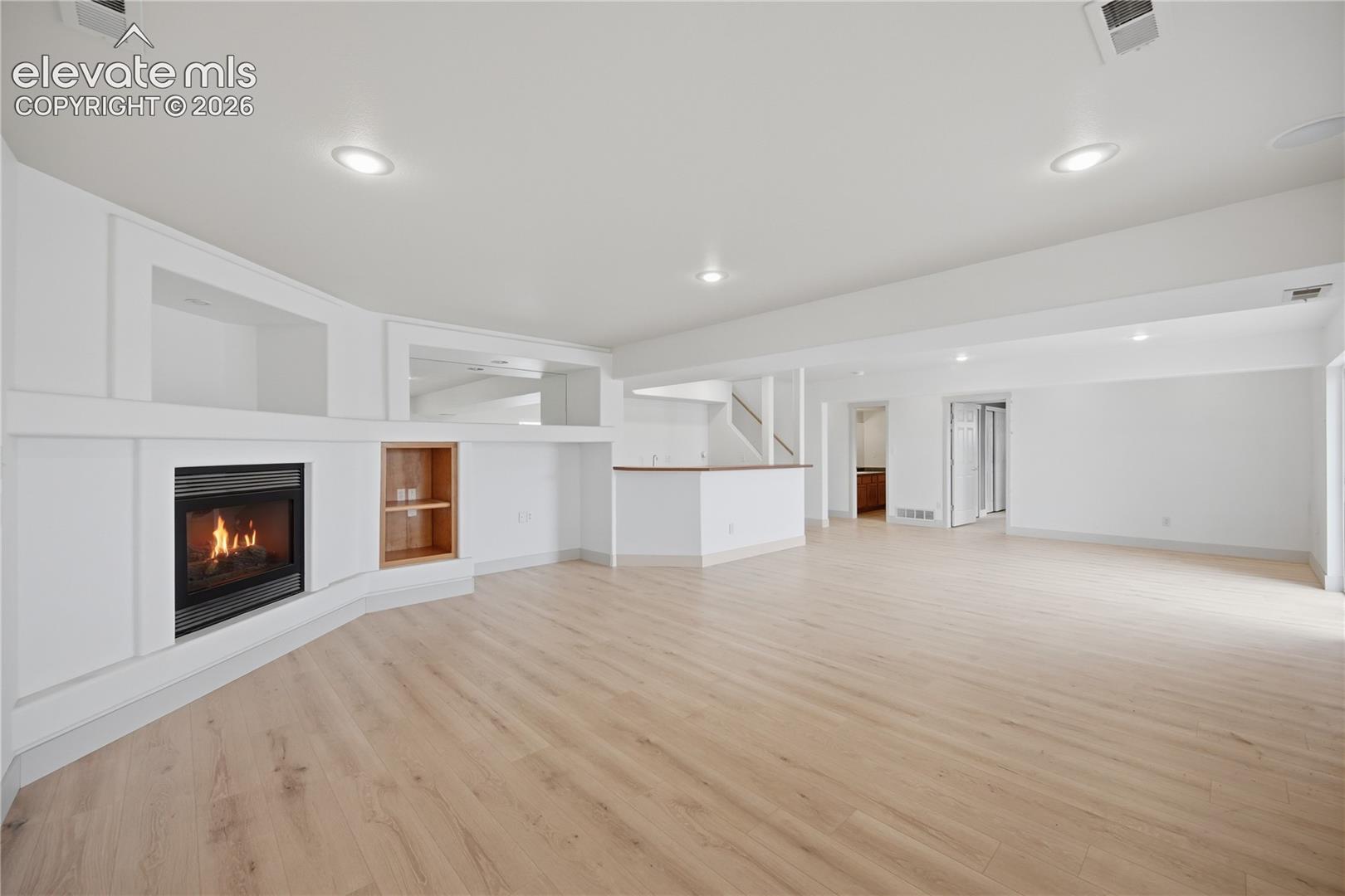 Spacious open interior featuring wood-finish flooring, recessed lighting, a built-in fireplace with custom shelving, and a peninsula-style counter