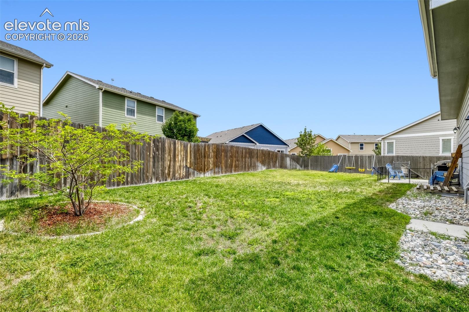 Expansive backyard featuring a manicured lawn, full privacy fencing, and a small tree with mulched surround