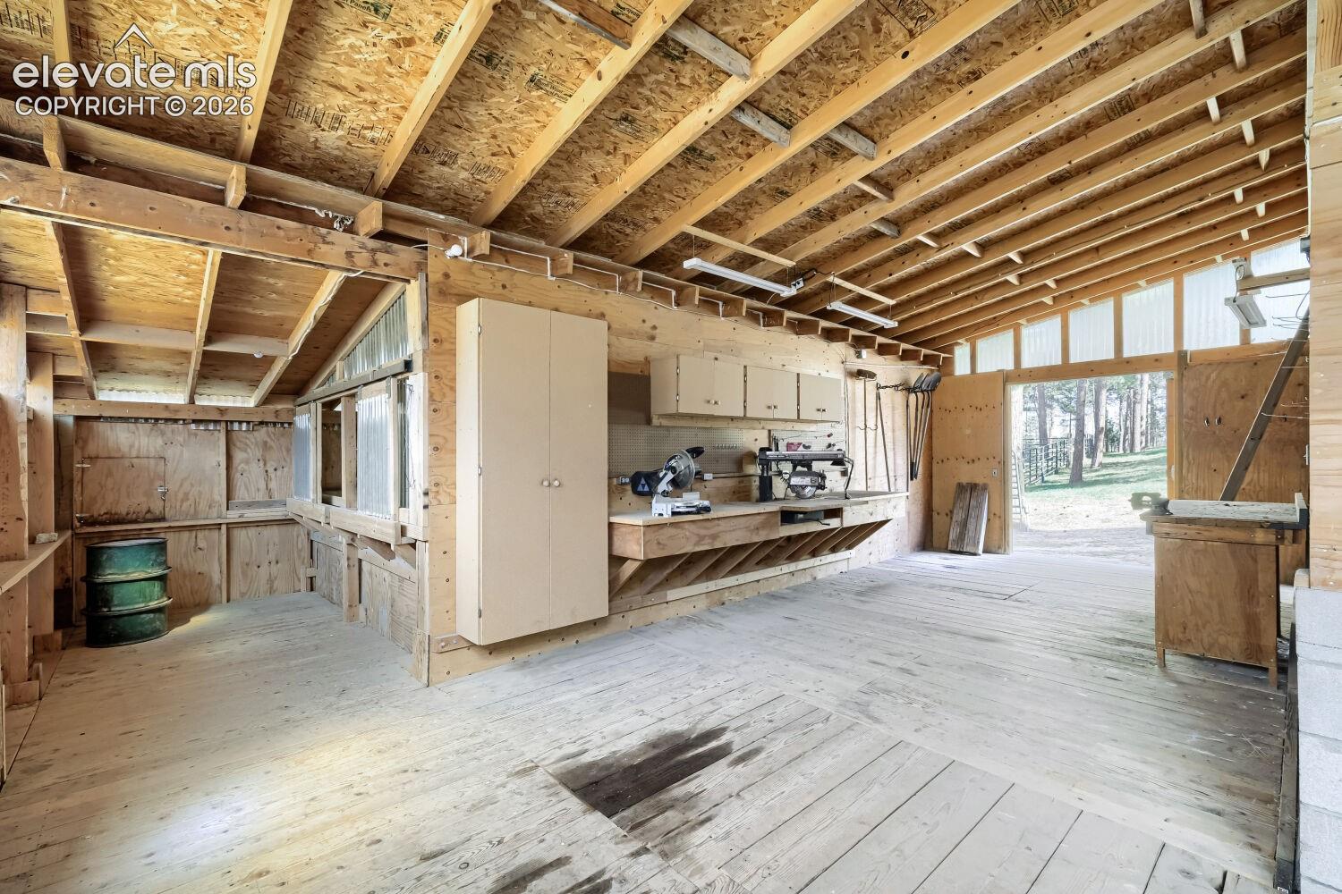 Wood-clad interior, exposed ceiling joists, built-in workbench with storage, wall-mounted cabinetry, and a large exterior opening