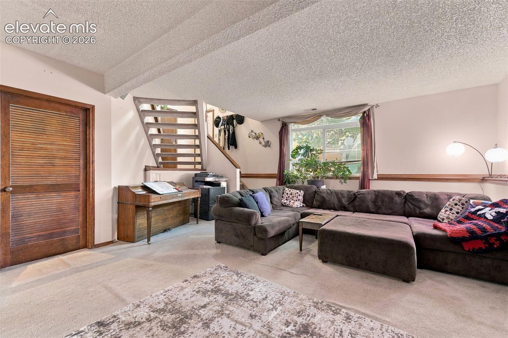 Living area featuring an open staircase with wood steps, a louvered wood-finish door, large picture window, and horizontal chair rail molding