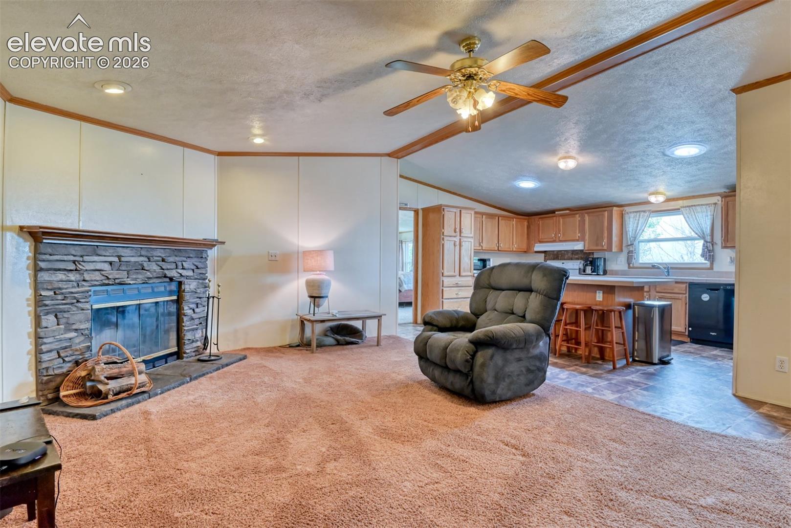 Living area featuring a stacked stone fireplace with a wood mantle, wood-finish ceiling fan, recessed lighting, and a neutral carpet