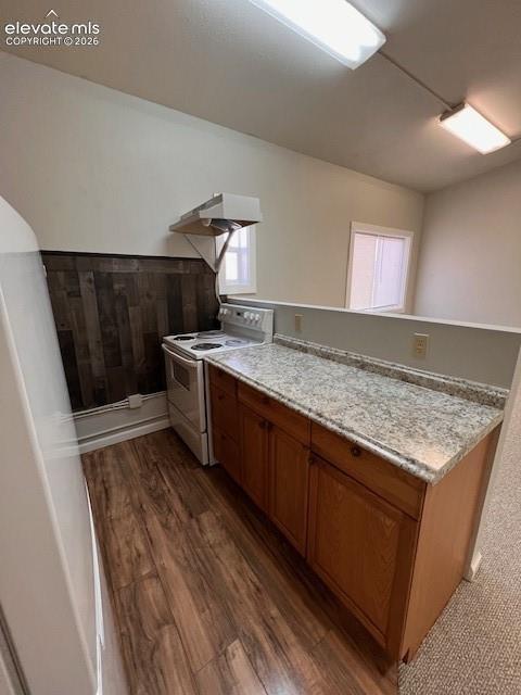Kitchen featuring wood-finish flooring, stone-patterned countertops, wood-finish cabinetry, a white electric range, and a decorative wood-panel accent wall