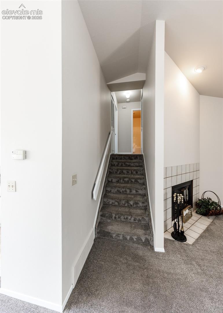 Carpeted staircase with white handrail, recessed lighting, and a tiled fireplace surround with hearth