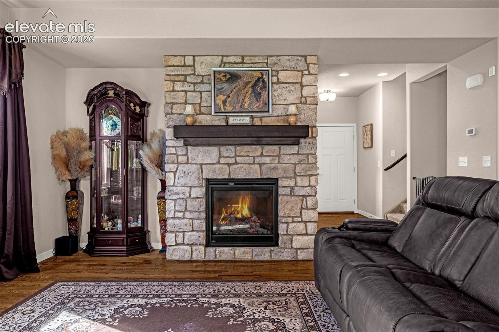 Floor-to-ceiling stone fireplace featuring a dark wood mantel and wood-finish flooring