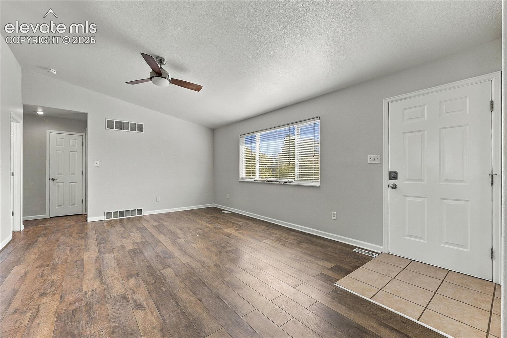 Interior space featuring wood-finish flooring, vaulted ceilings with a mounted paddle fan, a neutral color palette, and a tiled entryway