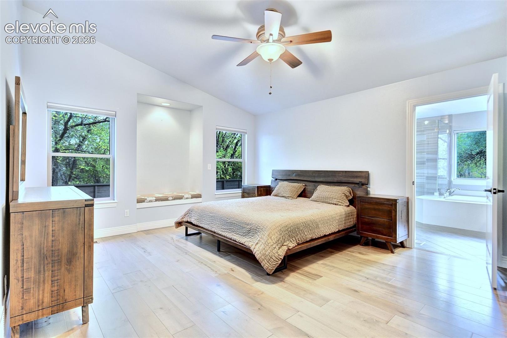 Vaulted ceiling with a central paddle fan, wood-finish flooring, recessed alcove with integrated lighting, and multiple windows