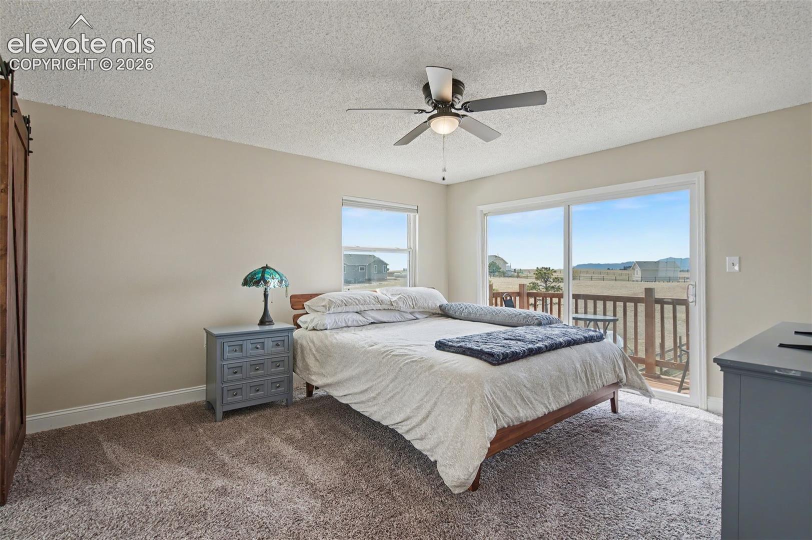 Room with neutral wall color, carpeting, ceiling fan with integrated light fixture, sliding glass door, and large window