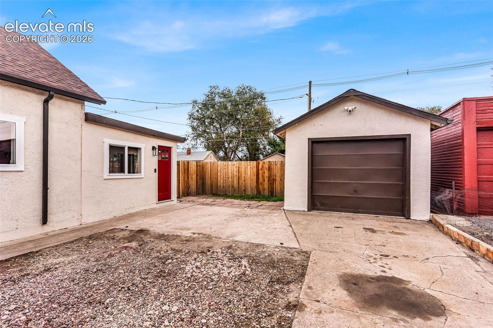 Stucco exterior featuring a detached single-car garage, concrete parking pad, and wood privacy fencing