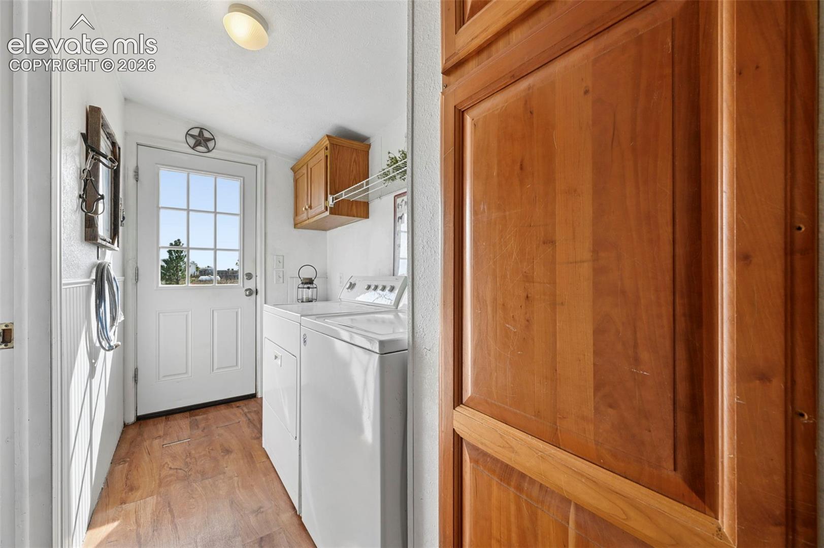 Utility space featuring wood-finish flooring, a white exterior door with glass pane, built-in wooden cabinetry, wall-mounted wire shelving, and beadboard wainscoting