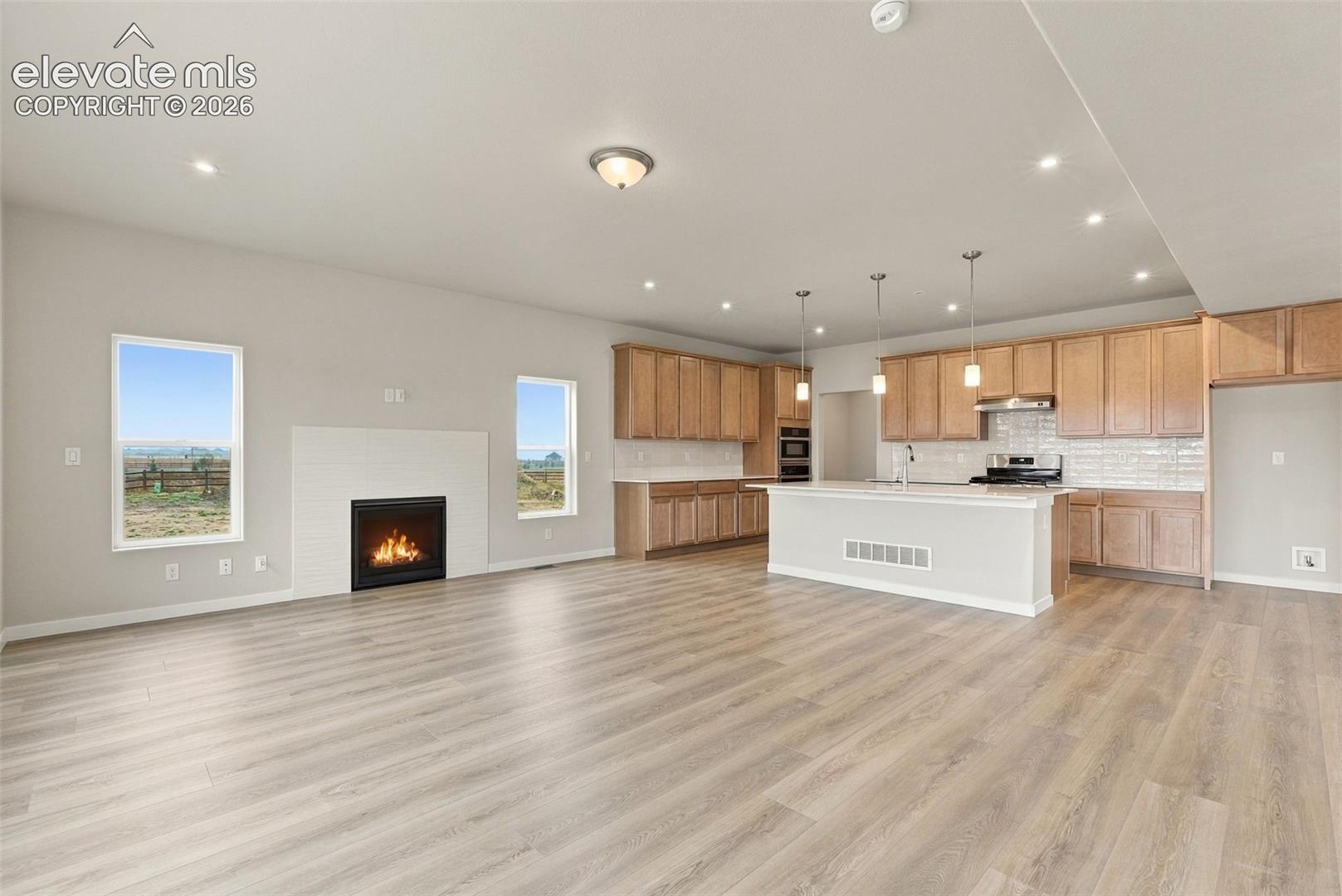 Open-concept kitchen featuring wood-finish cabinetry, a central island with pendant lighting, and tile backsplash