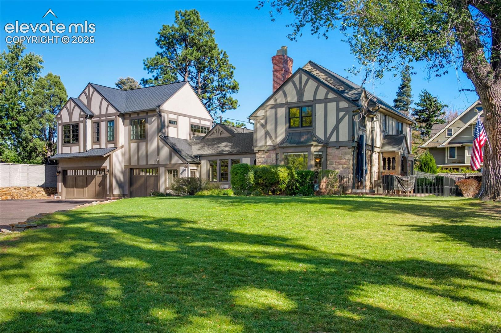 Tudor-style exterior featuring half-timbering, stone masonry, a steeply pitched roofline, an integrated multi-car garage, and a manicured lawn