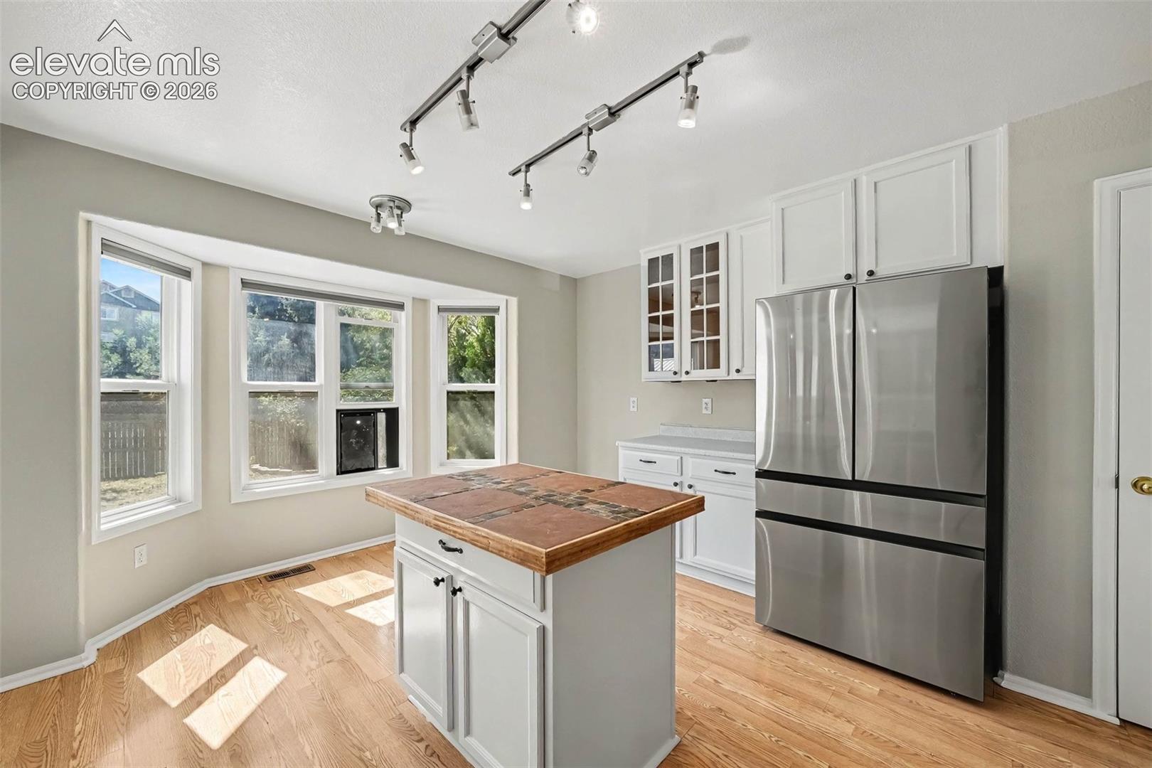Kitchen featuring wood-finish flooring, white cabinetry, stainless steel appliances, a kitchen island with a stone top, and multiple windows