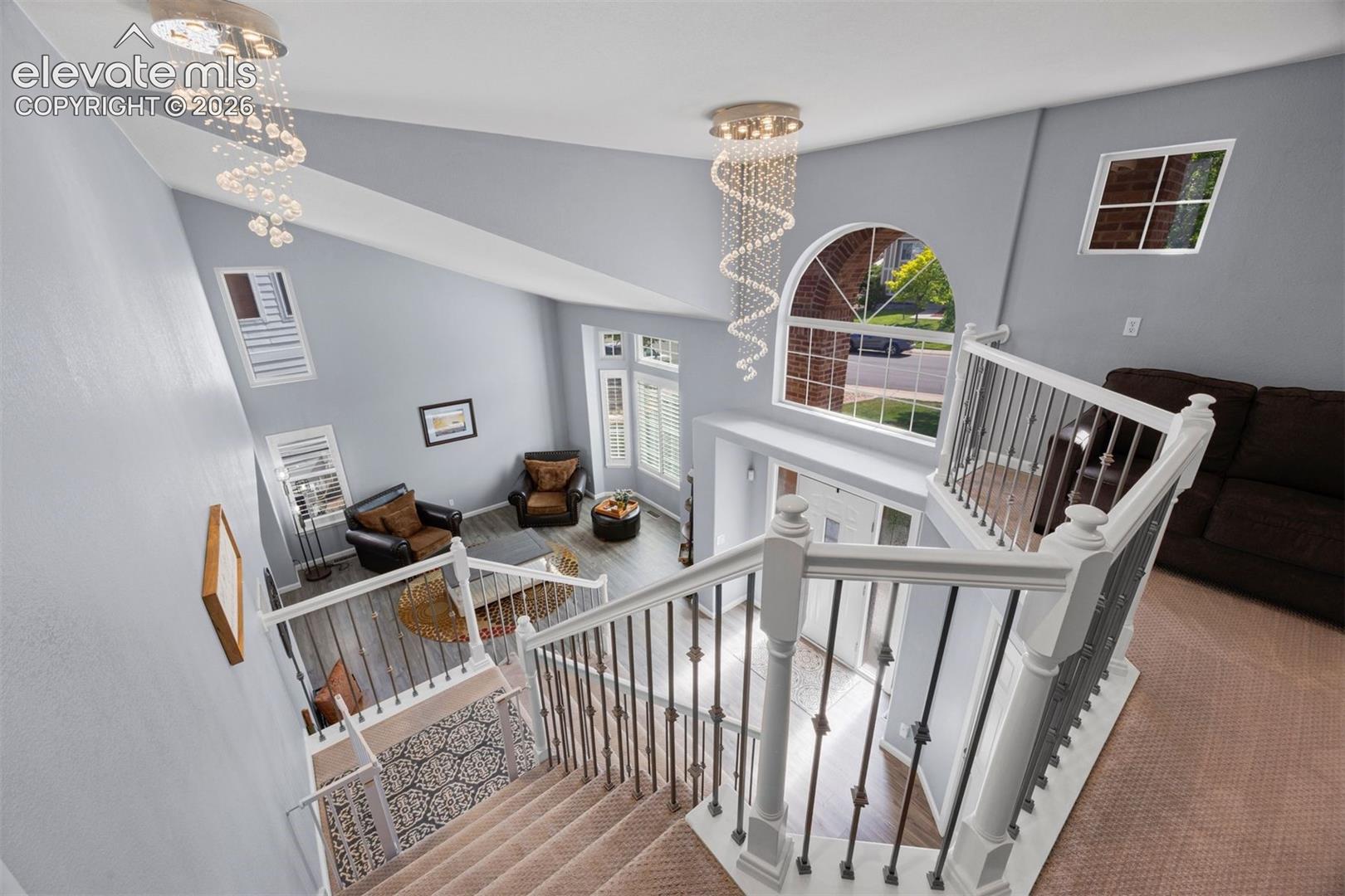 Foyer and living area showcasing a grand staircase, vaulted ceiling, and multiple windows including an arched window