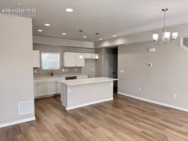 Open-concept space featuring wood-finish flooring, white cabinetry, a kitchen island with a white countertop, and recessed lighting