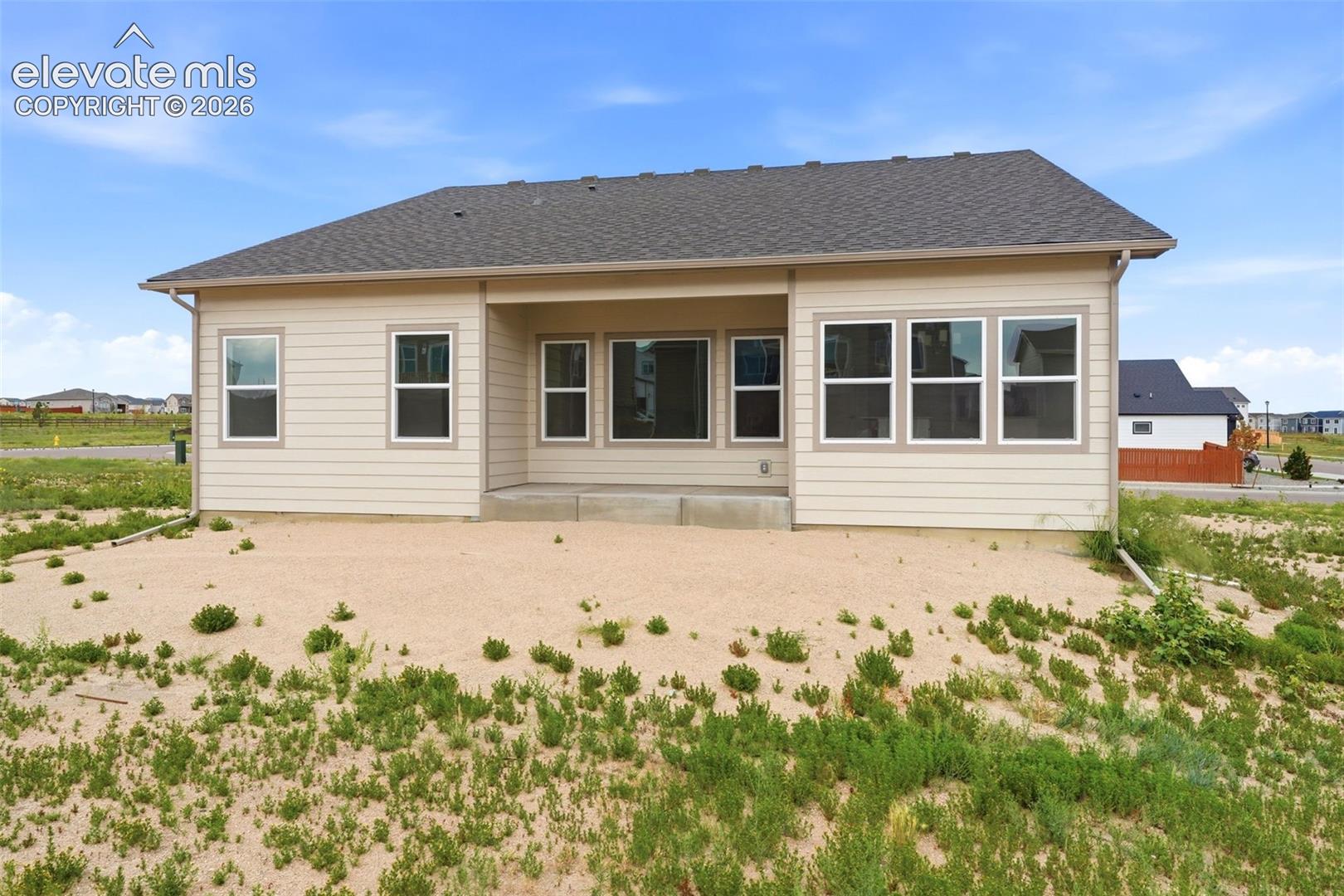Exterior rear elevation featuring horizontal siding, a gabled roofline, a covered concrete patio, and multiple energy-efficient window configurations
