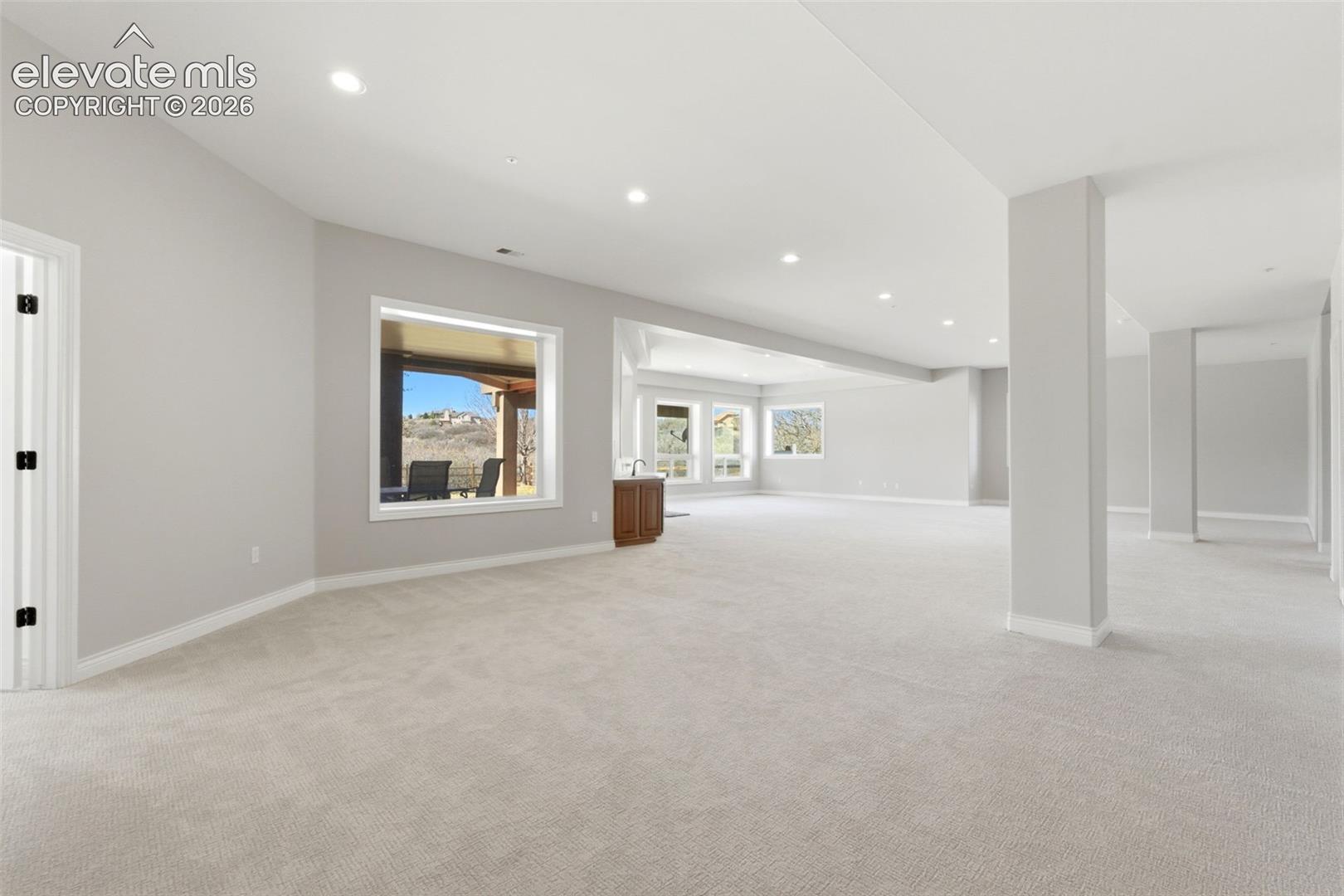 Expansive open room with neutral carpeting, recessed ceiling lighting, and multiple windows