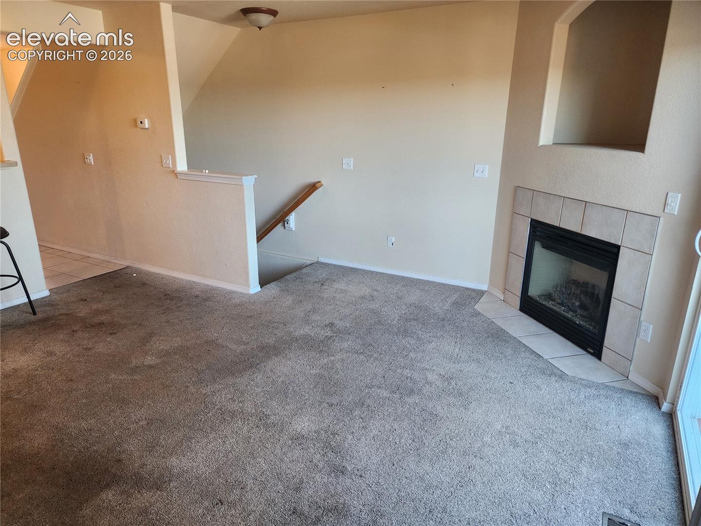 Carpeted living area with a corner-set fireplace featuring a tiled surround and an integrated niche