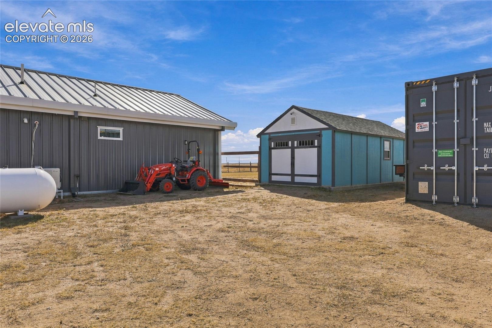 Exterior grounds featuring a metal-sided structure with a standing seam metal roof, a secondary detached outbuilding with double doors, and a steel shipping container