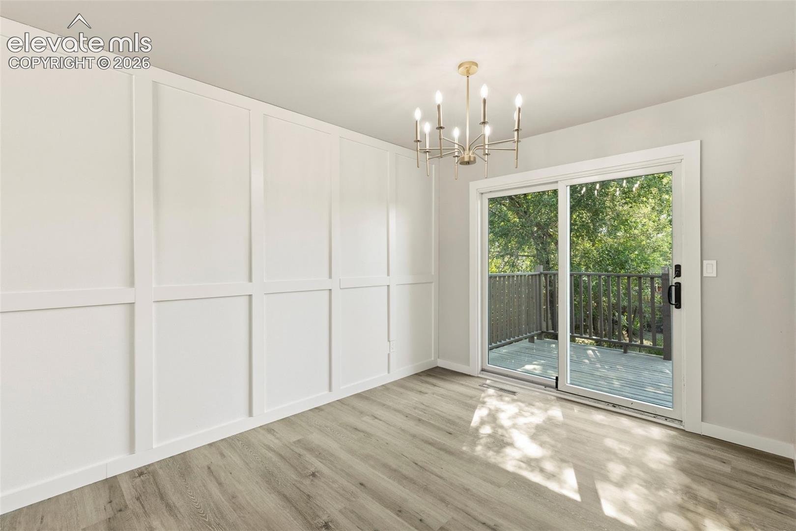 Interior space featuring board and batten wall paneling, a contemporary chandelier, luxury vinyl plank flooring, and a sliding glass door opening to an exterior deck