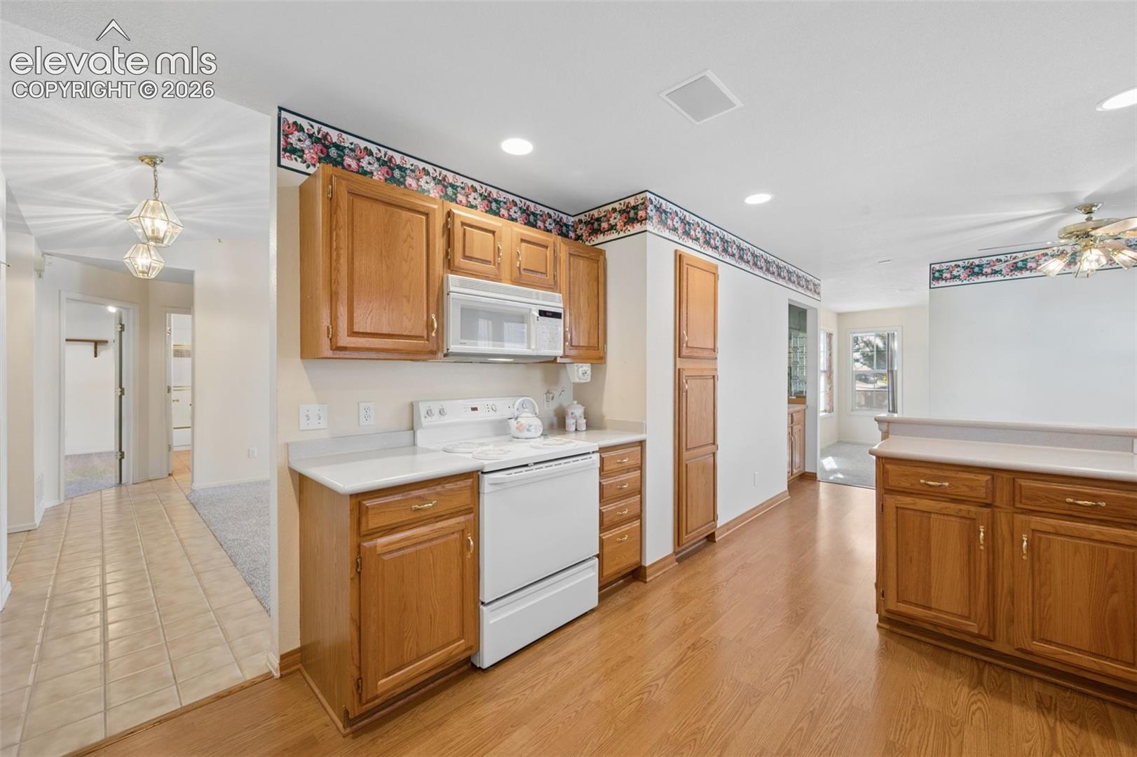 Kitchen featuring oak-finish cabinetry, white appliances, solid-surface countertops, and wood-finish flooring