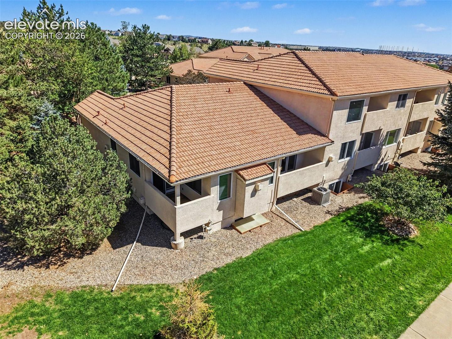 Terracotta tile roof, stucco exterior, multiple balconies, mature trees, and a manicured lawn