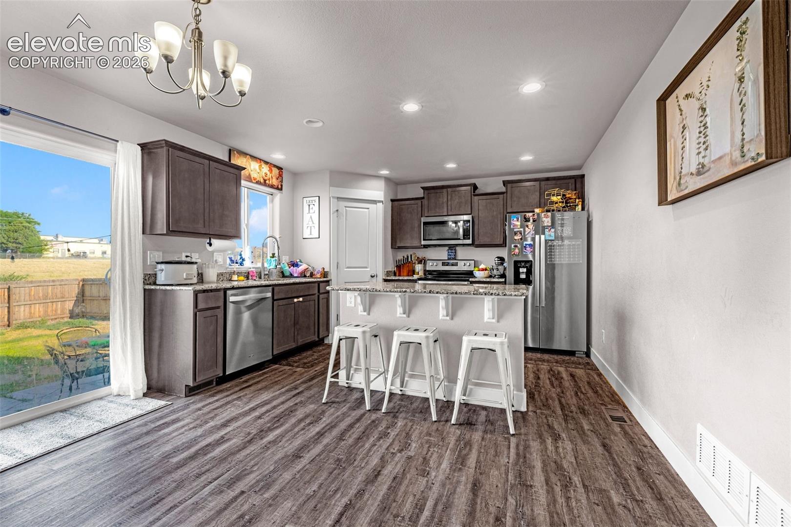 Open-concept kitchen featuring wood-finish flooring, dark wood cabinetry, stainless steel appliances, and a central island with bar seating