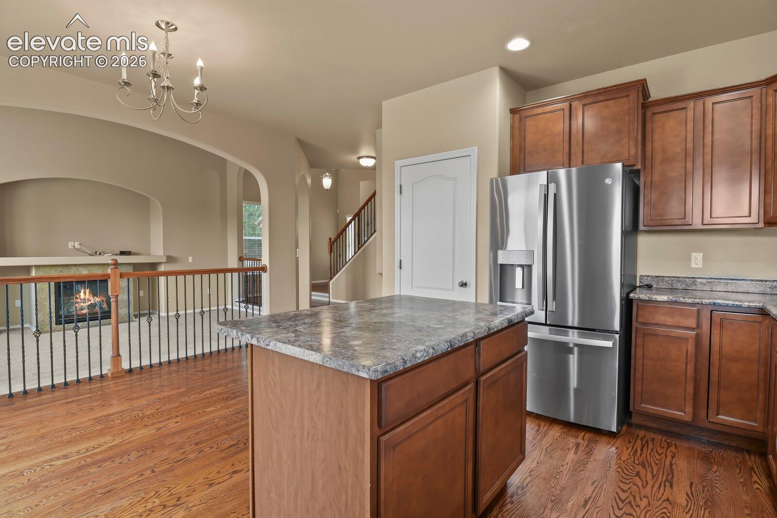 Kitchen featuring wood cabinetry, stainless steel refrigerator, and a central island with a stone-finish countertop