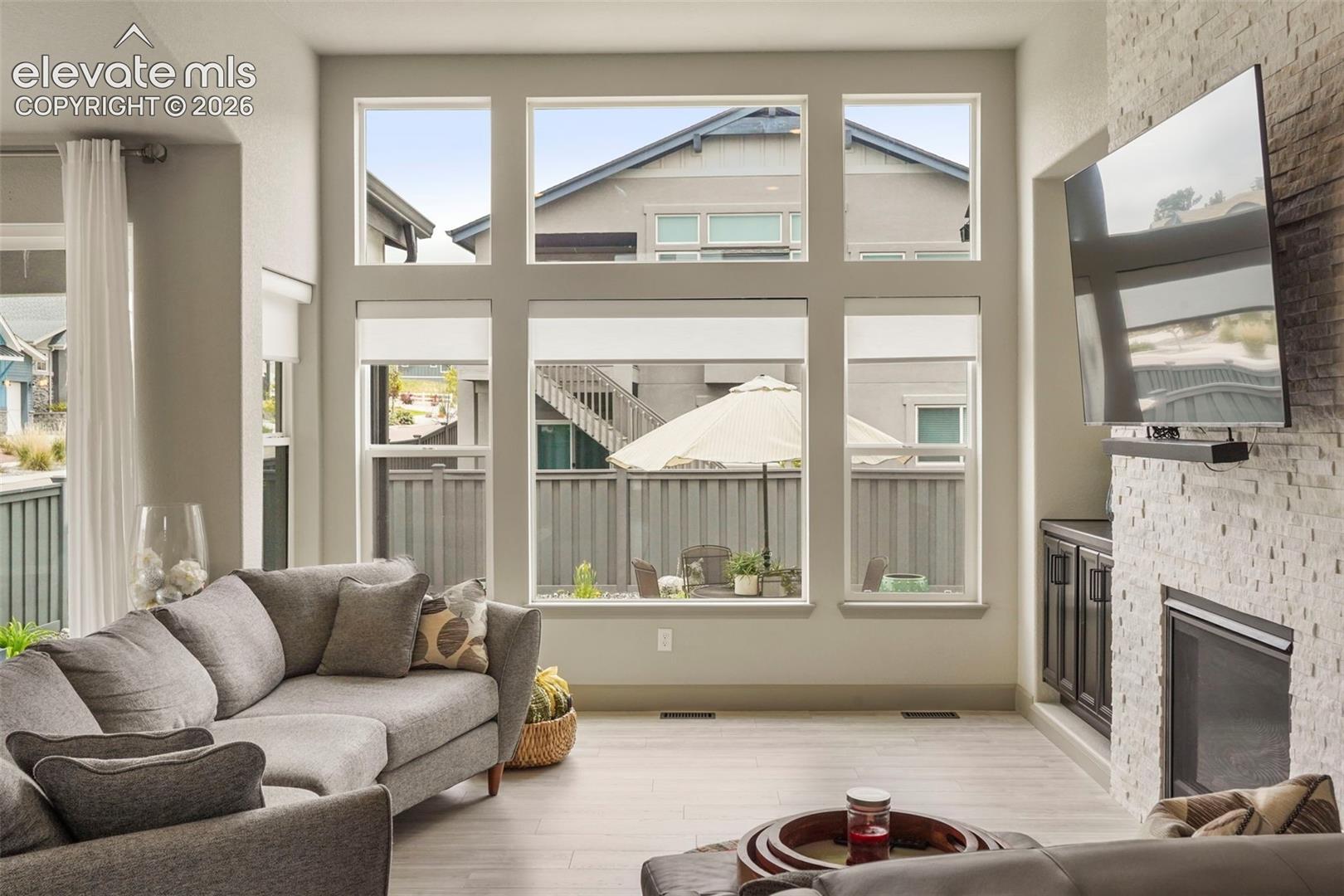 Living area featuring a floor-to-ceiling window arrangement with multiple panes, light wood-finish flooring, a contemporary fireplace with stacked stone surround, and built-in cabinetry