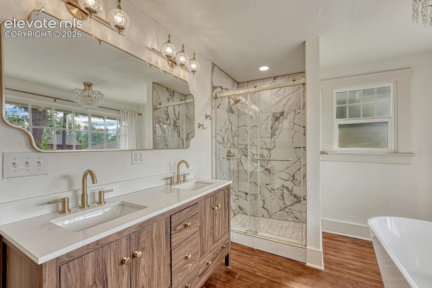 Dual vanity with wood-finish cabinetry, quartz countertop, and brass fixtures