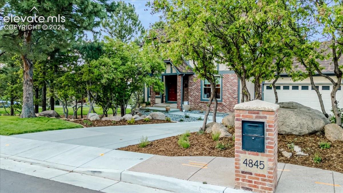 Brick and stucco exterior with an attached garage, featuring a concrete driveway and natural landscaping