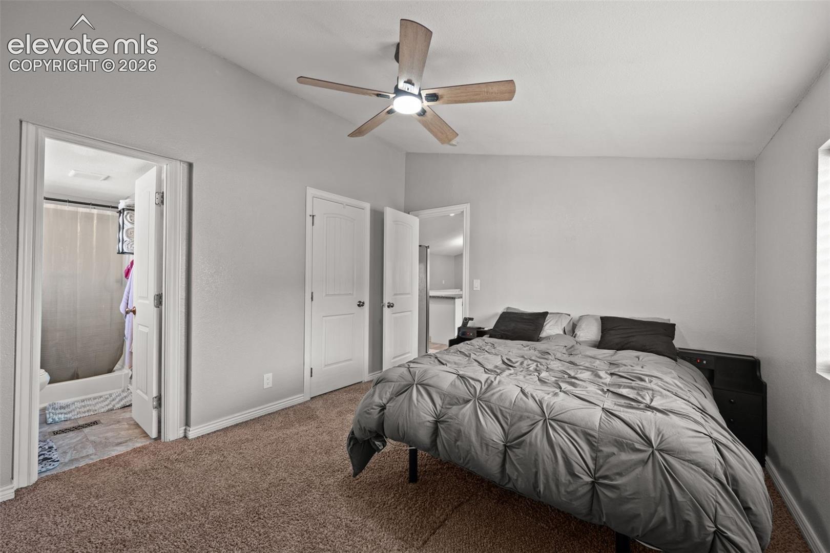 Neutral-toned interior featuring vaulted ceilings, carpeting, multi-blade ceiling fan with integrated lighting, and white interior doors