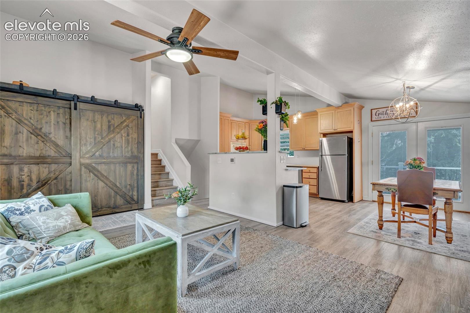 Open-concept living area featuring wood-finish flooring, a contemporary ceiling fan, and exposed structural beams