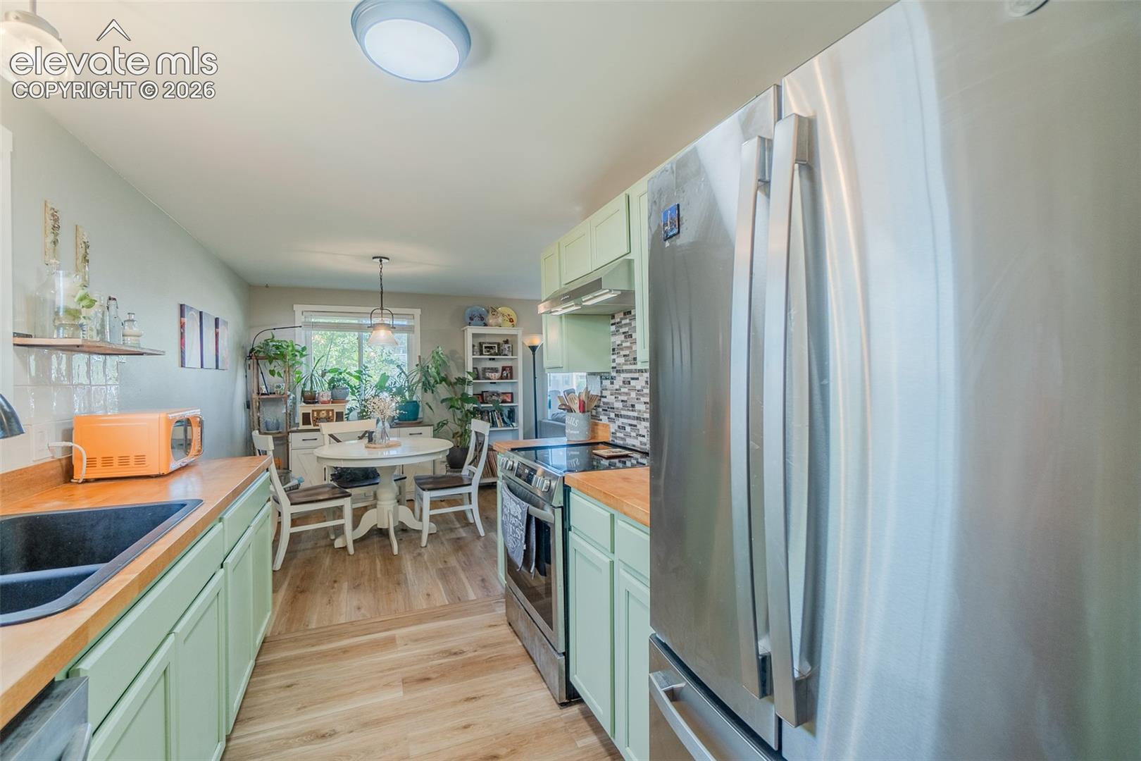 Kitchen featuring light green cabinetry, wood-finish countertops, and stainless steel appliances
