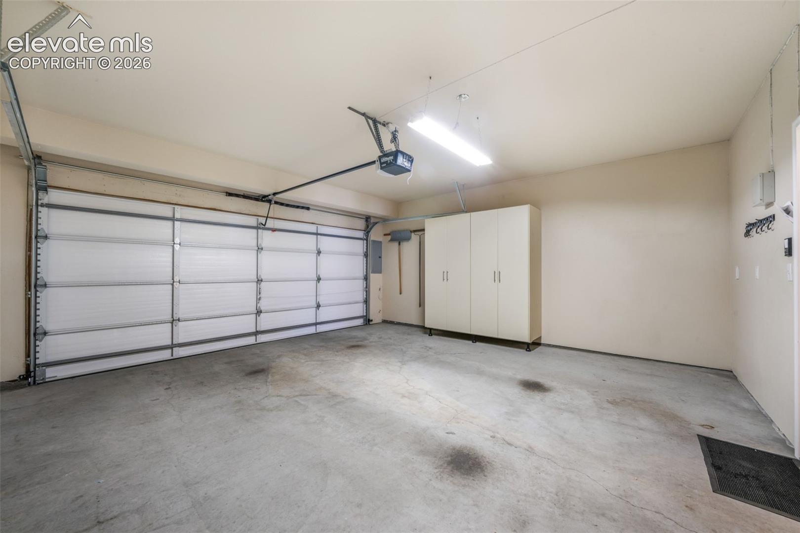 Attached garage with concrete flooring, built-in storage cabinetry, and overhead lighting