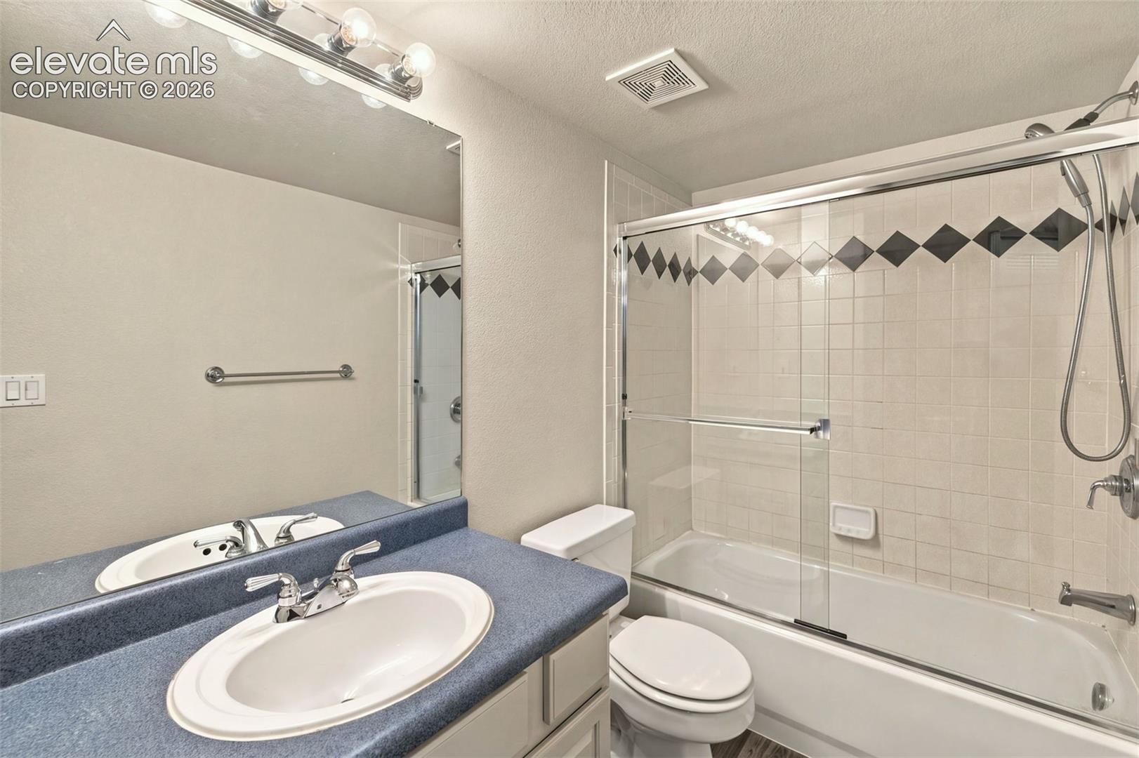 Bathroom featuring a vanity with an integrated basin, a large wall-mounted mirror, a tub-shower combination with a sliding glass door, and tiled wall accents