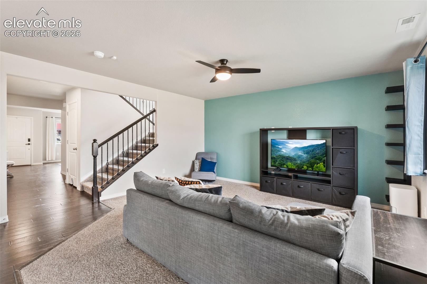 Open-concept living space with dark wood-finish flooring, a carpeted living area, and a staircase with a dark wood handrail and metal balusters
