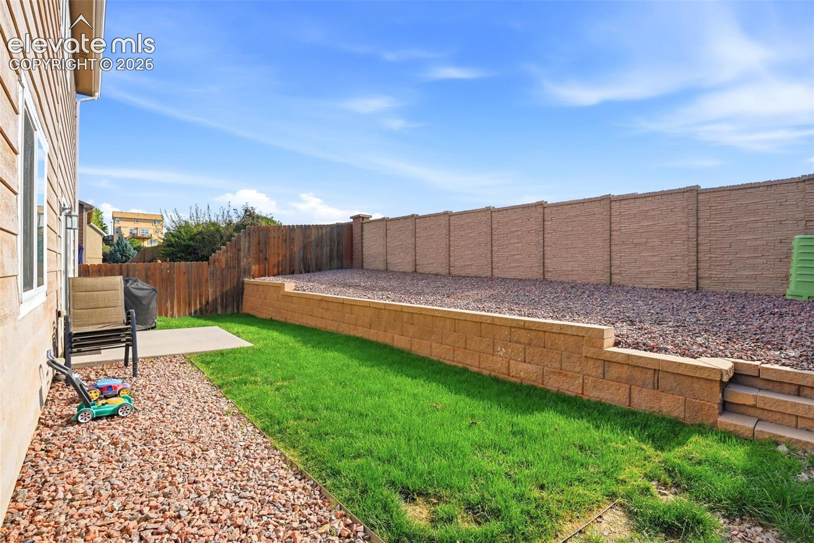 Private backyard featuring a concrete patio, retaining wall with integrated steps, and a combination of natural rock and grass landscaping