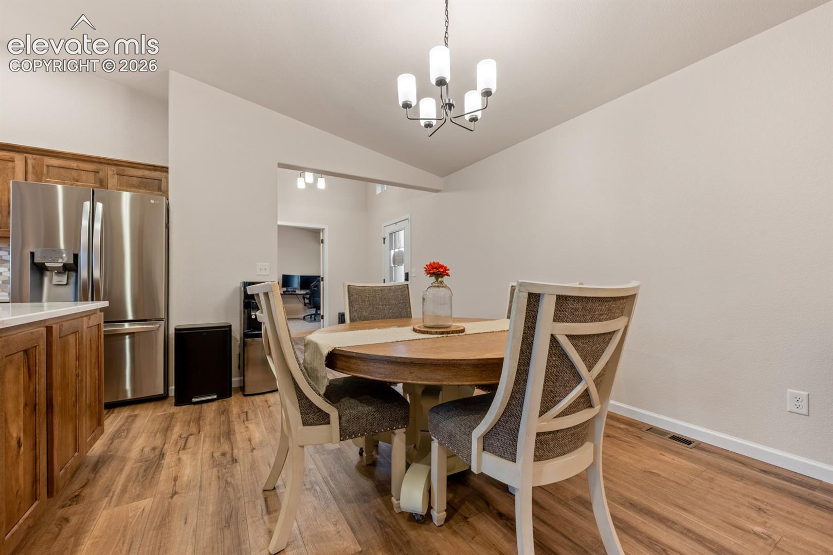Wood-finish flooring, stainless steel refrigerator, white cabinetry, and multi-light chandelier fixture