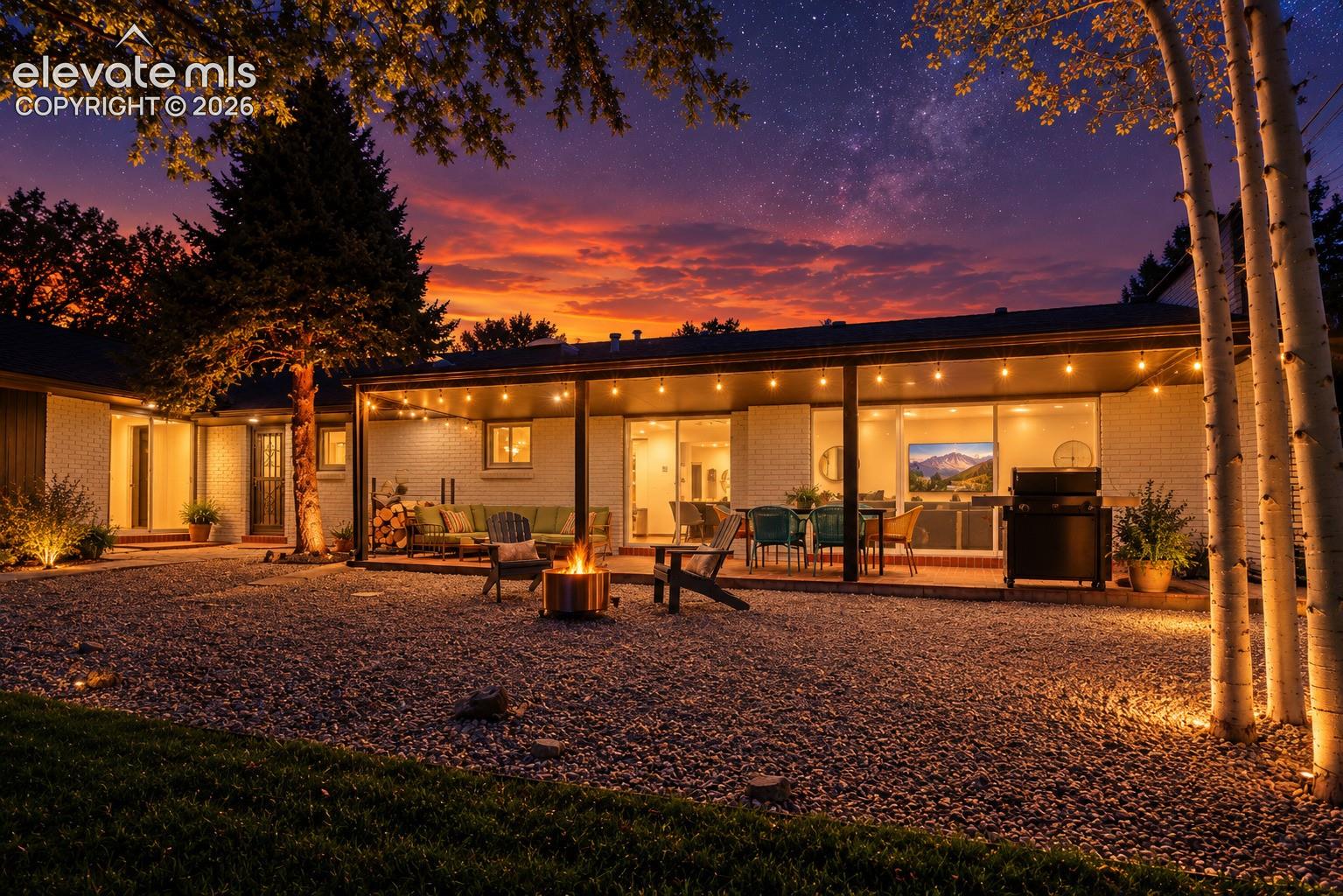 Extensive gravel yard with perimeter landscaping, covered patio featuring string lighting, and large sliding glass doors