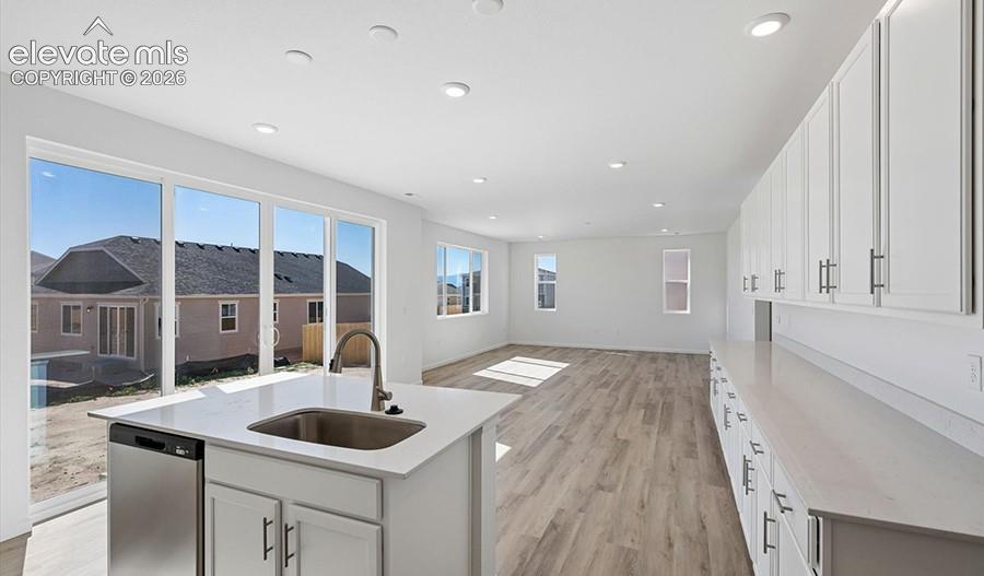 Kitchen featuring white shaker-style cabinetry, solid-surface countertops, recessed lighting, wood-finish flooring, and a stainless steel under-mount sink